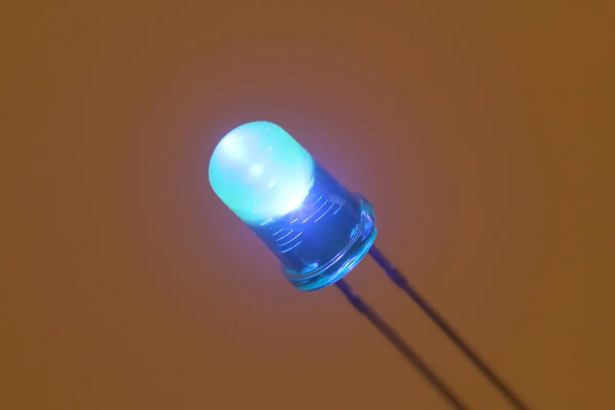 A small blue LED with two long metal legs, glowing bright blue