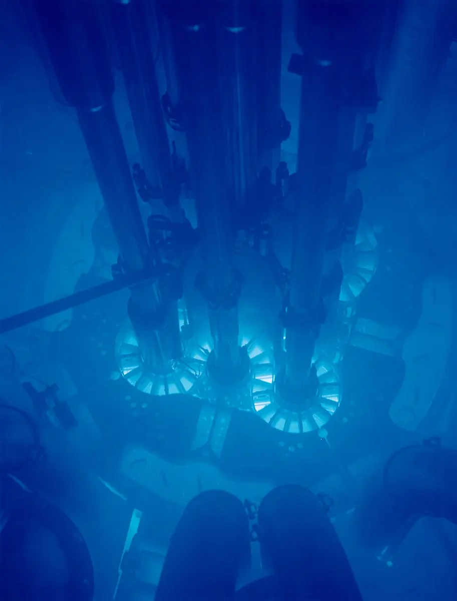 Looking down into deep water at the core of a nuclear reactor, with round shapes of equipment glowing bright blue