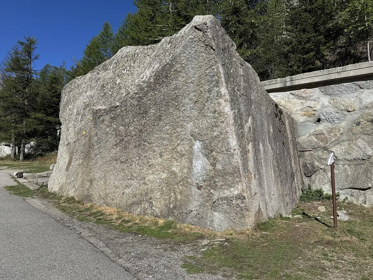 A huge block of gray granite beside a mountain road, with pine trees behind it