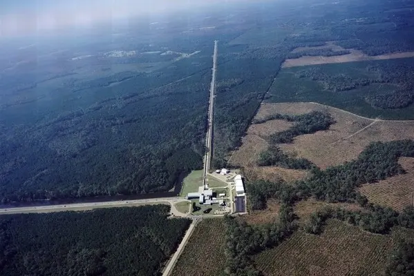 An aerial photograph of green forest with two long straight cleared lines meeting at right angles at a group of white buildings