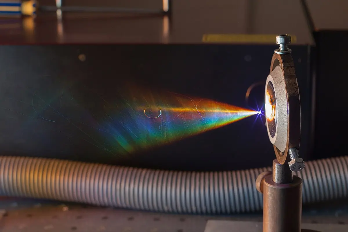 A laser beam focused to a point in the air makes a bright white spark, from which a fan of rainbow colors spreads out onto a dark background