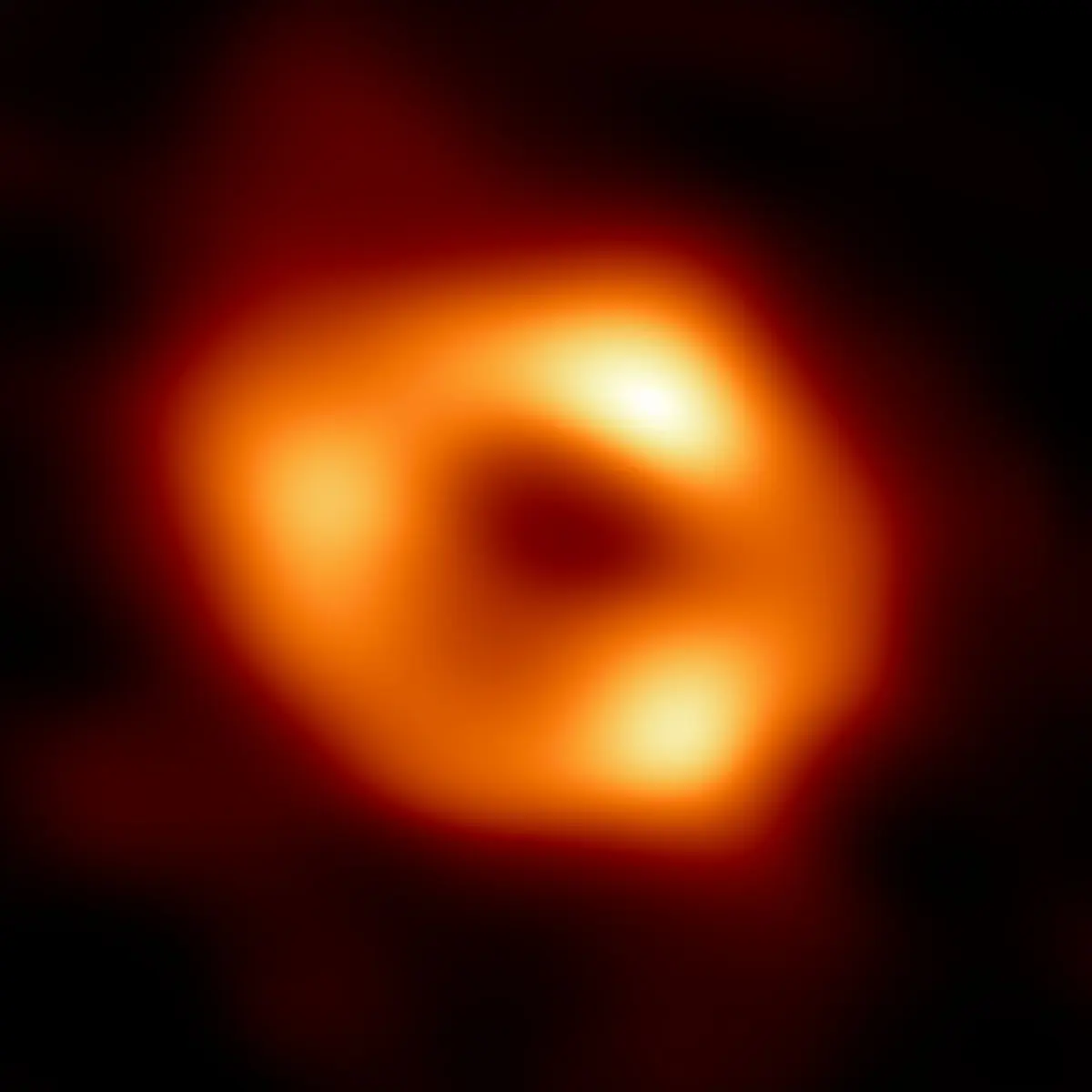 A blurry orange ring of light, brighter in three places, around a dark center, on black