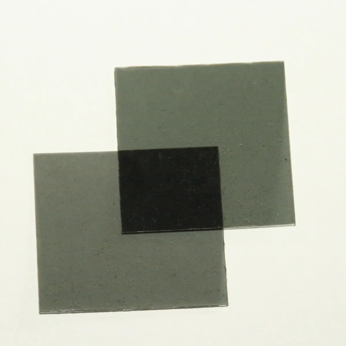 Two gray see-through squares of plastic film overlapping at one corner. Where they overlap, the square is almost black.