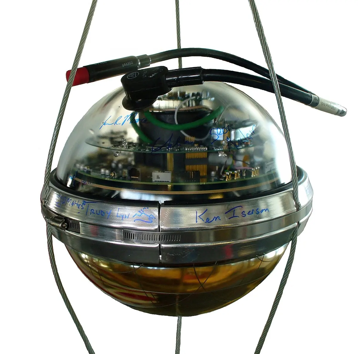 A glass sphere hanging in a harness of steel wires, with circuit boards visible through its upper half, a metal band round its middle signed in marker pen, and a black cable plugged into its top