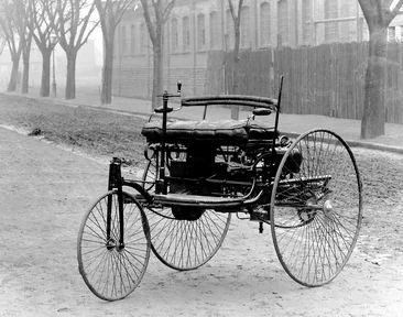 An early three-wheeled car with large spoked wheels, a bench seat and no roof