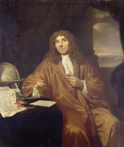 A painted portrait of Antonie van Leeuwenhoek sitting at a table, holding a small microscope