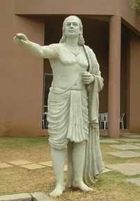 A white statue of Aryabhata, standing barefoot and pointing to the sky