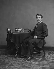 Thomas Edison sitting beside his early phonograph