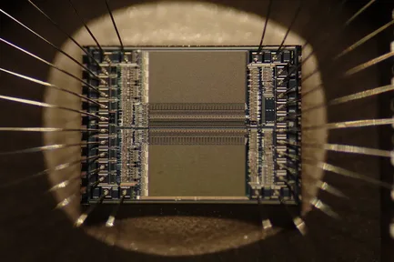 A close-up of a microchip, with tiny silver wires joining the chip to its legs