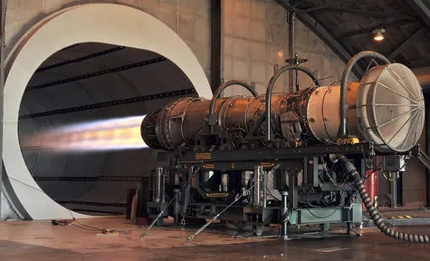 A jet engine on a test stand, its exhaust glowing orange
