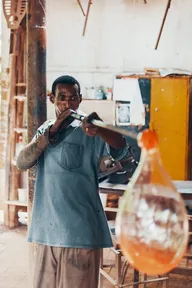 A glassblower shaping a glowing bubble of hot glass on the end of a tube
