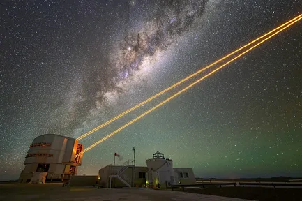 Four orange laser beams shining up into the night sky from a telescope in Chile, under the Milky Way