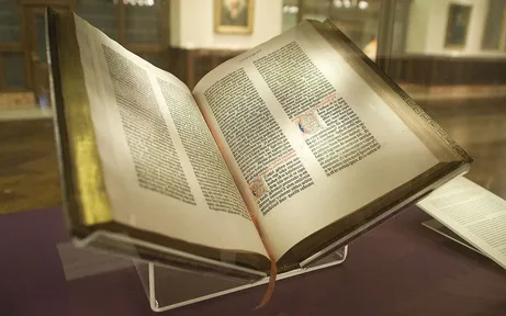 An open Gutenberg Bible with two columns of black Latin letters on each page