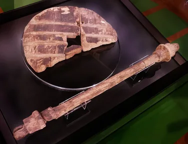 A large, round wooden wheel made of planks, dark with age, with its wooden axle