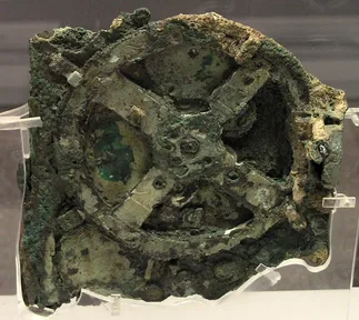 A flat lump of corroded bronze with the outlines of gearwheels inside it
