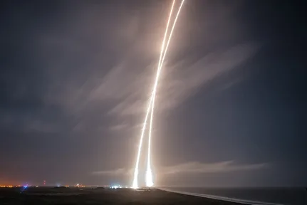 A long-exposure night photo with two streaks of light: the rocket going up, and its booster coming back down to land near the launch site