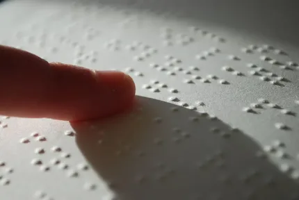 Fingertips reading a page of raised braille dots