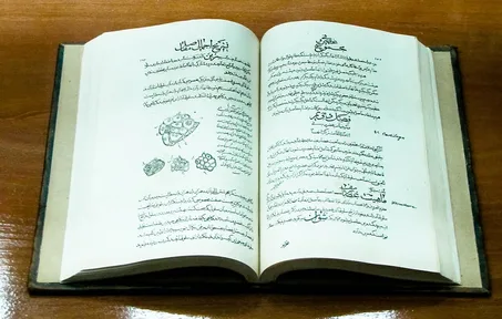 An open handwritten copy of the Canon of Medicine in Persian, in a museum case