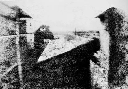 A blurry gray picture of rooftops and buildings seen from an upstairs window