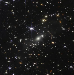 Webb’s First Deep Field: thousands of galaxies, some stretched into arcs, on a black sky