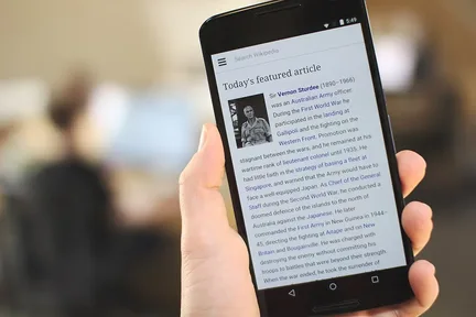 A hand holding a smartphone showing a web page